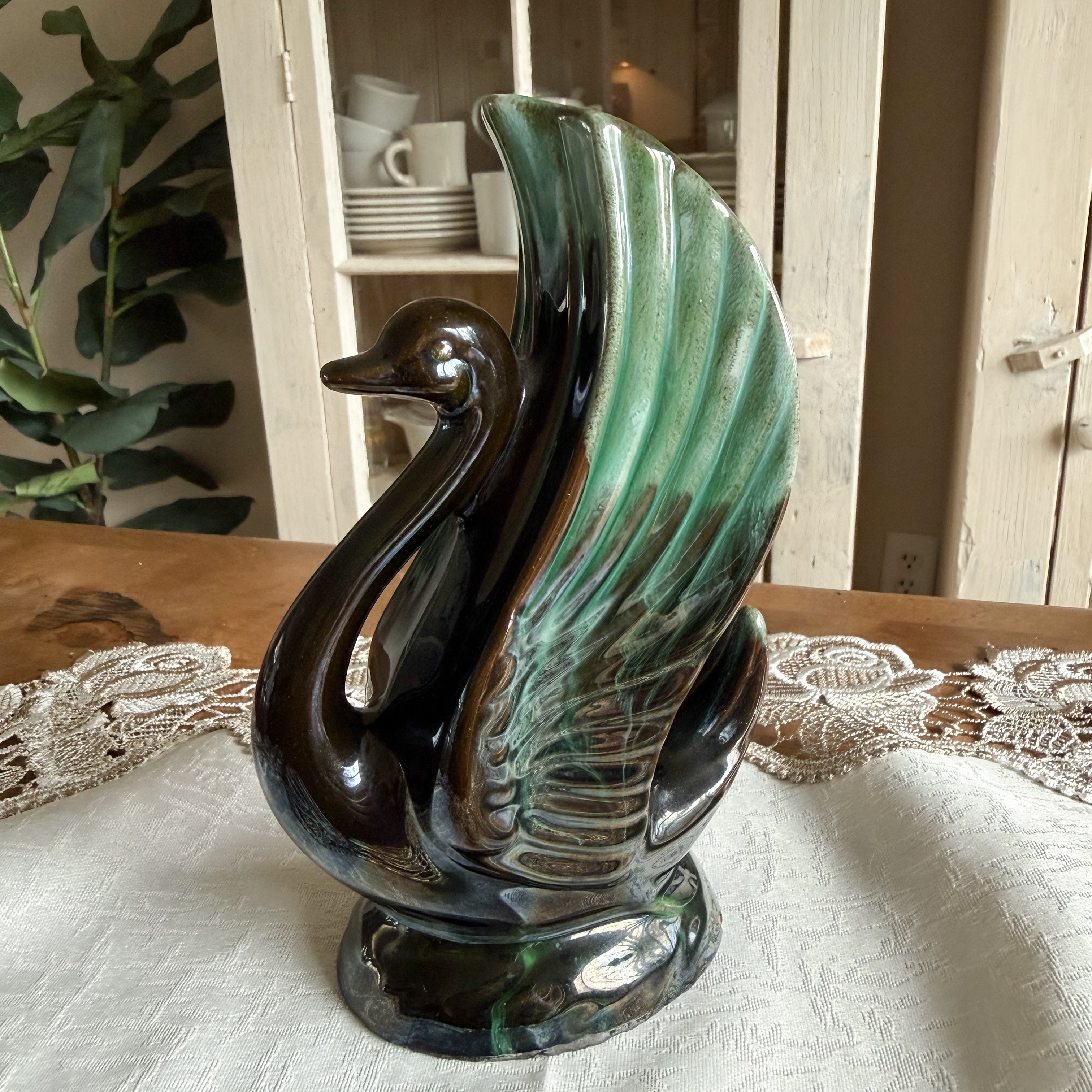 Side profile of a vintage ceramic swan vase with a high, flared wing and green drip glaze.