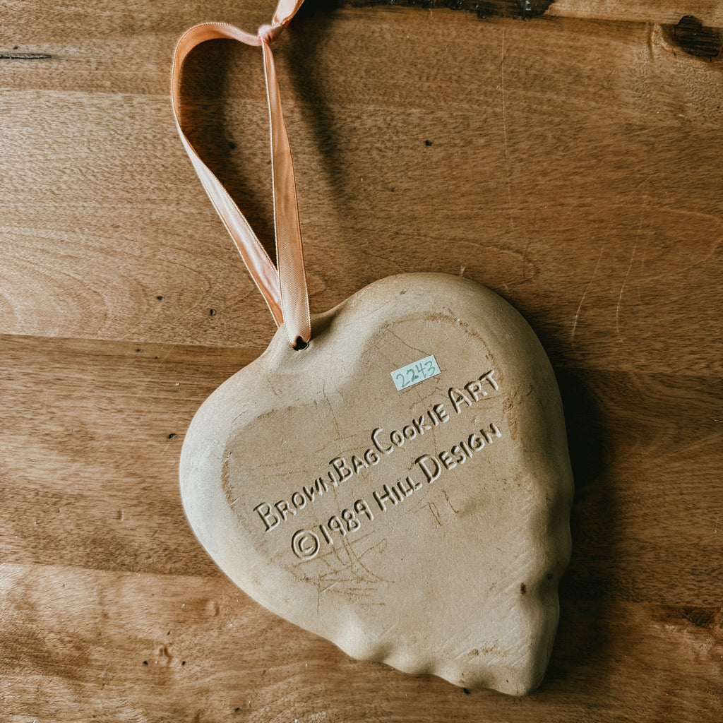 Back side of A tan-colored, heart-shaped stoneware cookie mold with Brown Bag Cookie Art marked in 1989 Hill Design
