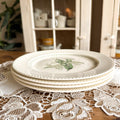 A stack of four vintage Royal China Waverly dinner plates on a lace tablecloth with a farmhouse cabinet background.