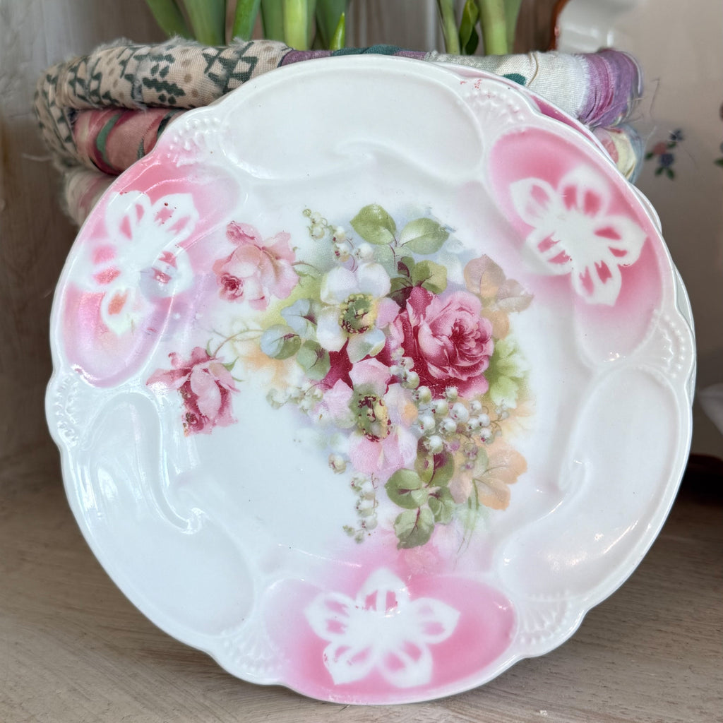 Antique German porcelain dessert plate featuring a central bouquet of pink roses and white lilies with a scalloped edge and pink airbrushed borders.