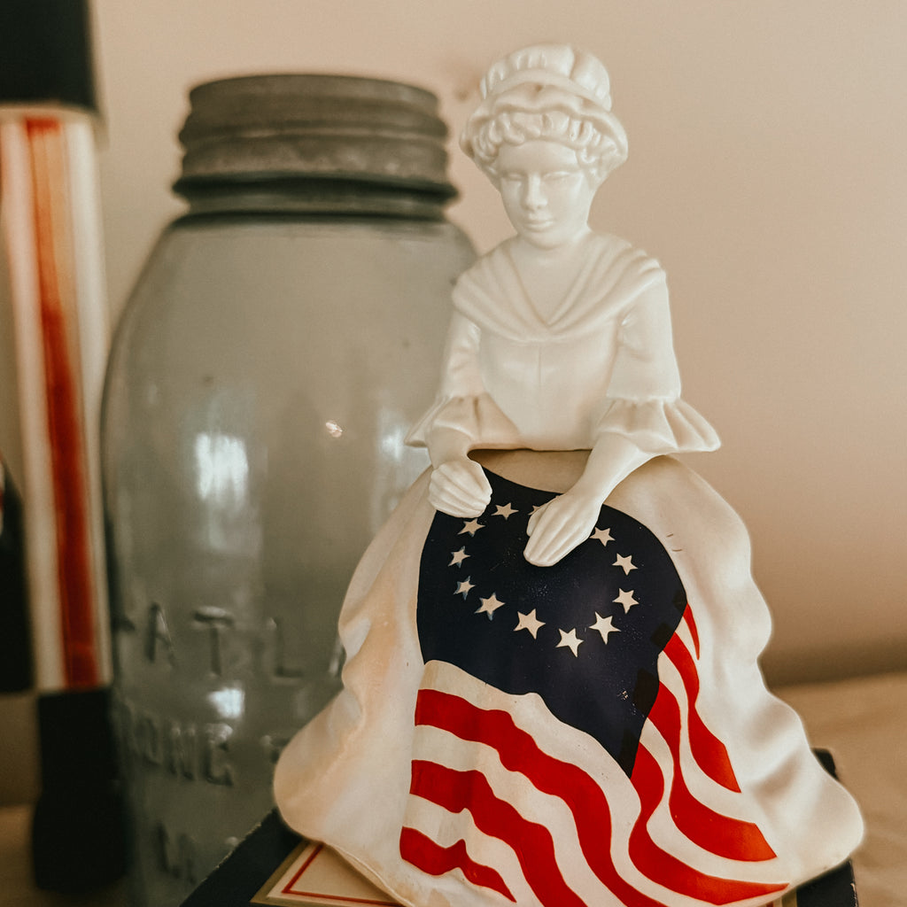 Close-up of a 1970s Avon Betsy Ross matte white glass decanter featuring hand-painted details and colonial dress.