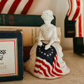Vintage 1976 Avon Betsy Ross milk glass figurine cologne bottle standing next to its original blue illustrated retail box.