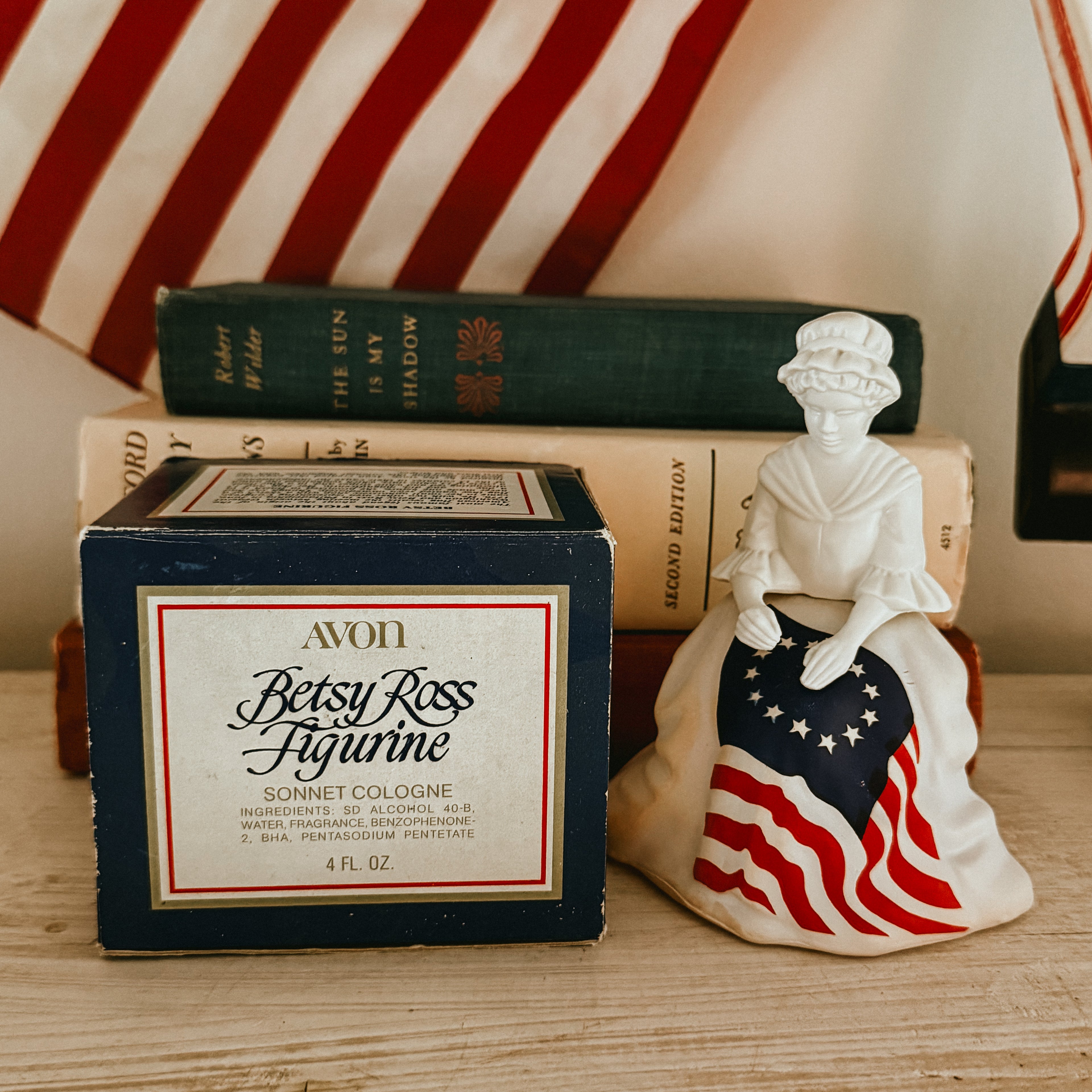 Vintage 1976 Avon Betsy Ross milk glass figurine cologne bottle standing next to its original blue illustrated retail box.